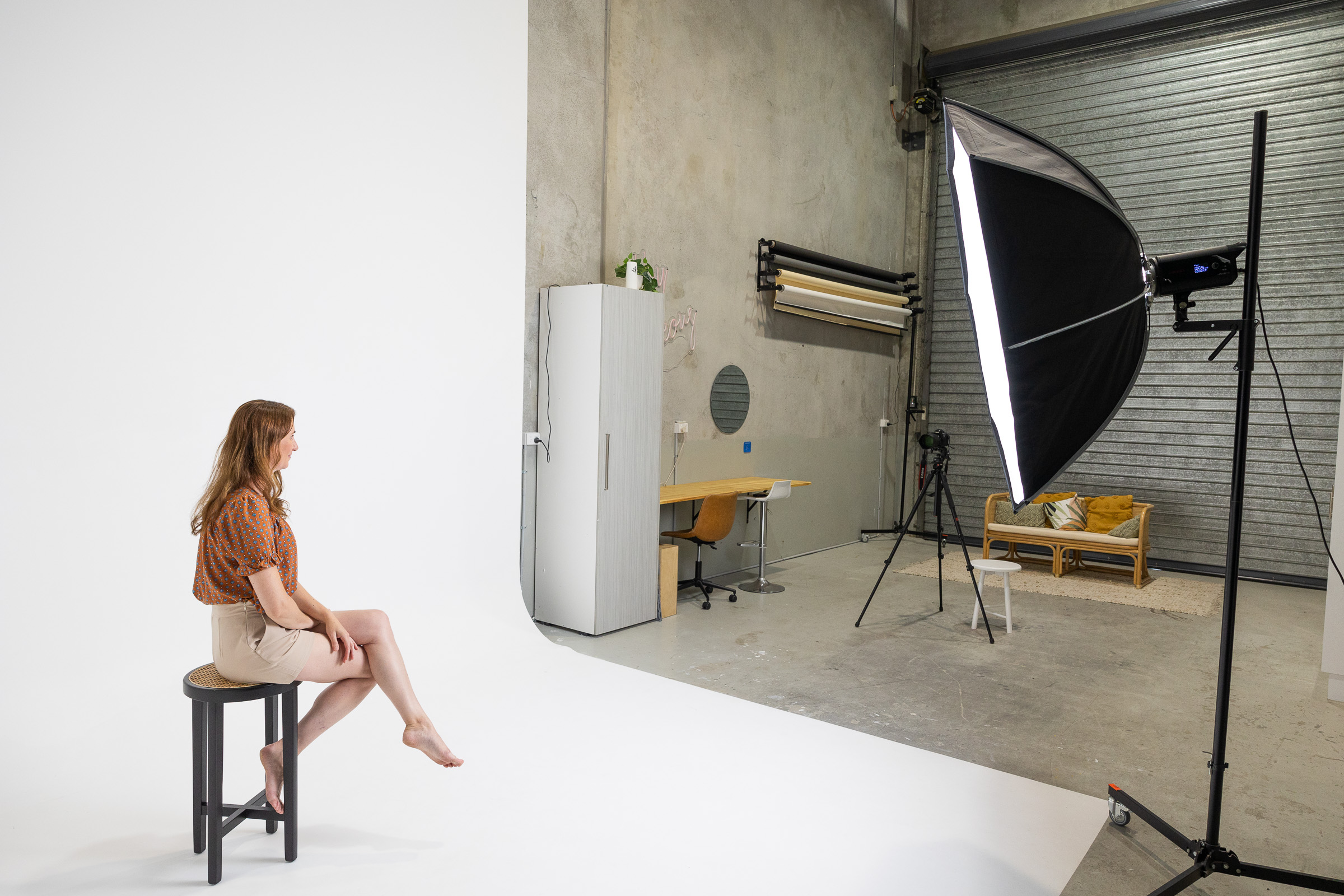 image shows full length of brilliant white hire studio with white corner cyclorama and large soft box lighting, production desk, paper backdrop system and client seating.